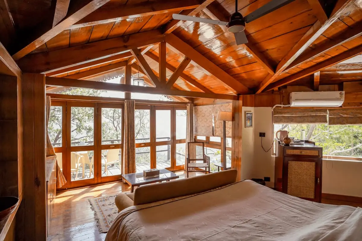 Bed facing forest-view windows under timber trusses in the Superior Cottage Room, Two Chimneys Gethia